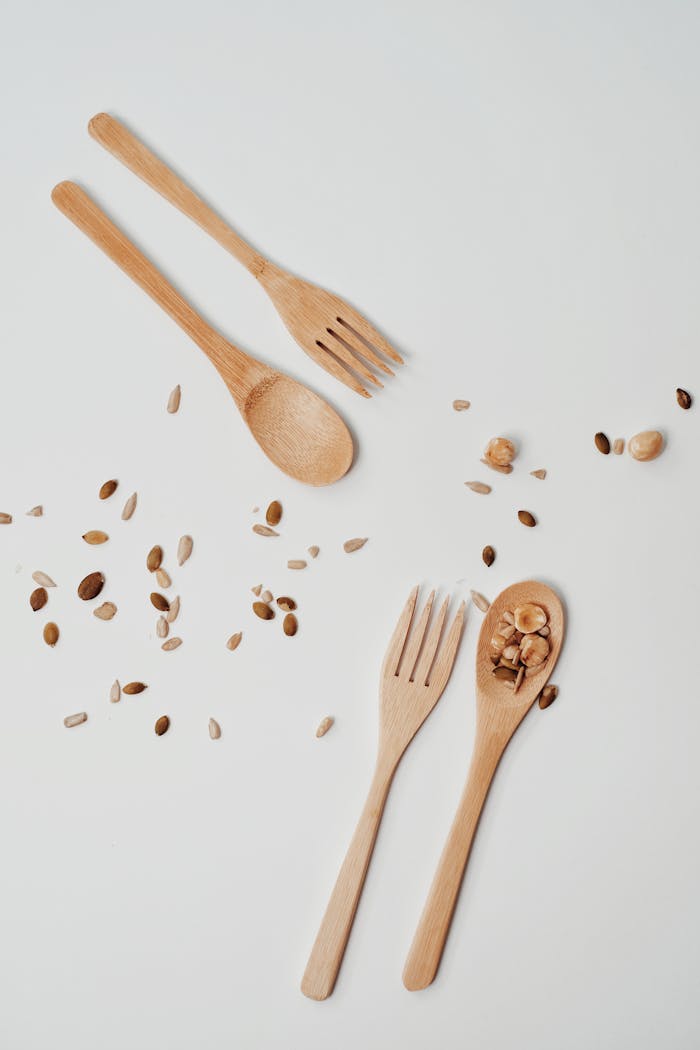 Wooden forks and spoons with scattered seeds on a white background, showcasing sustainable dining.